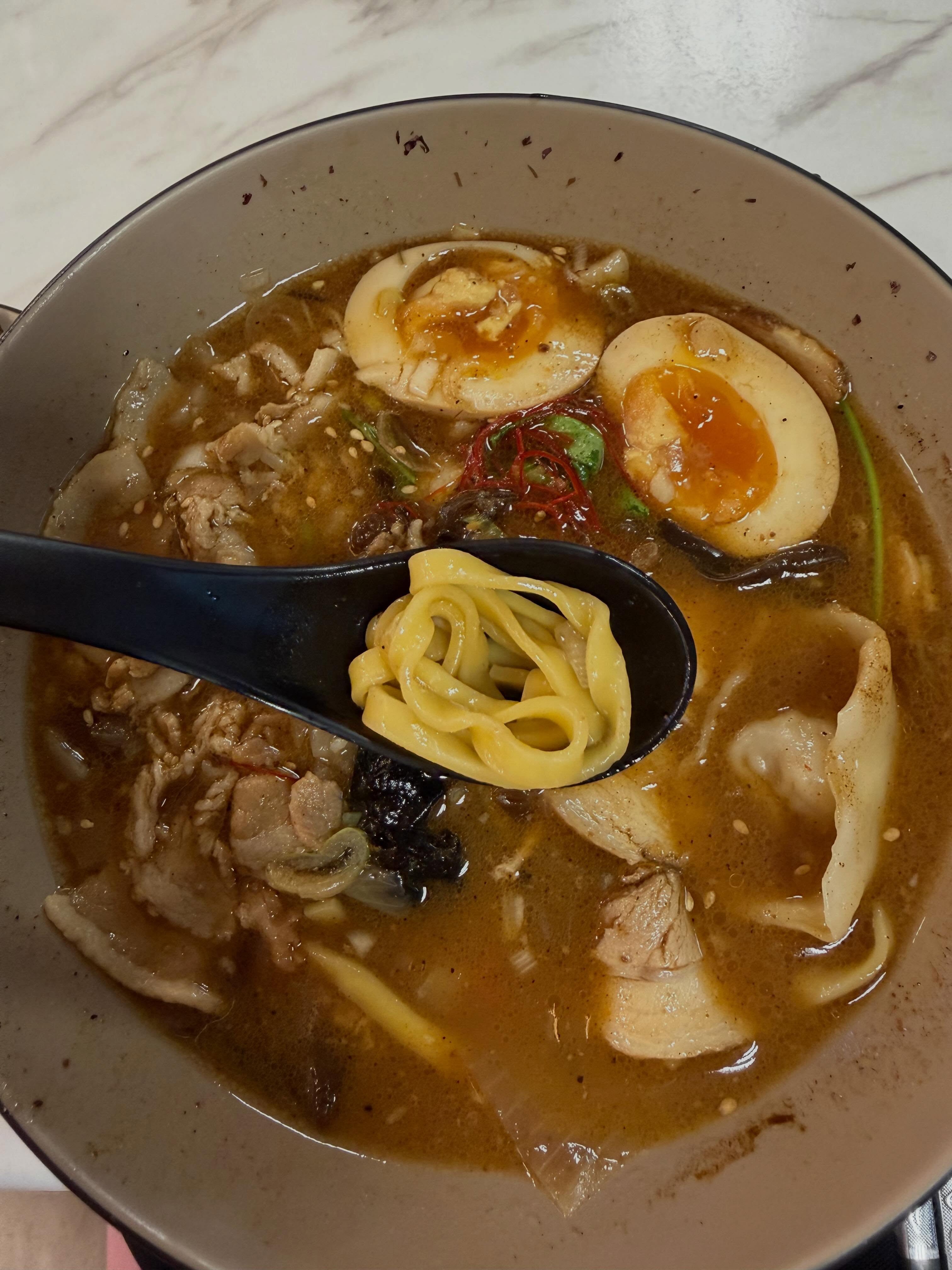 Top-down shot of Black Gold King Ramen with noodles, ajitama, pork, and dumplings in dark broth